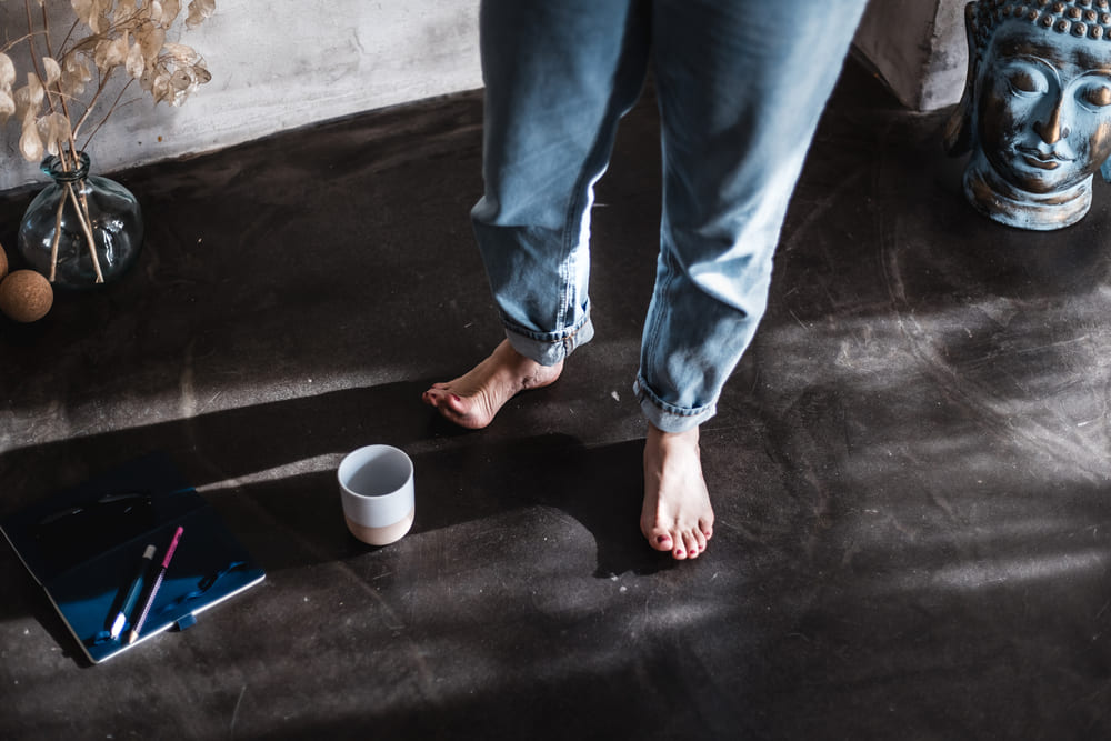 Vesna Zivanic barfuß im Achtsamkeitsraum mit Notizbuch, Tasse und Buddha – Symbol für Bodenständigkeit, Ruhe und Reflexion