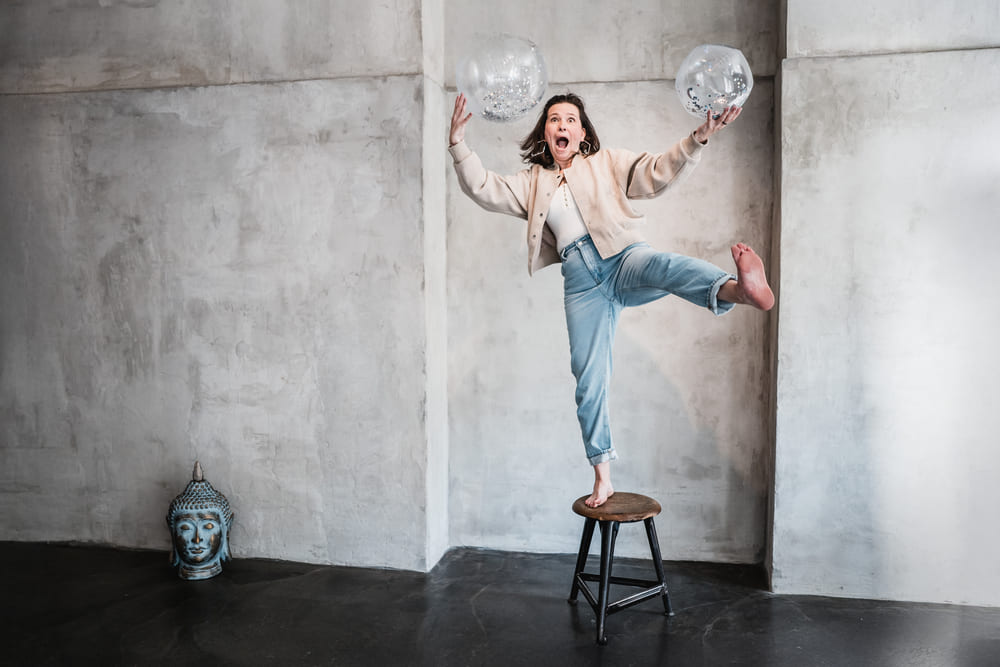 Vesna Zivanic balanciert spielerisch auf einem Hocker mit zwei Bällen – Symbol für Balance, Kreativität und Stressbewältigung bei Impulspaket.de